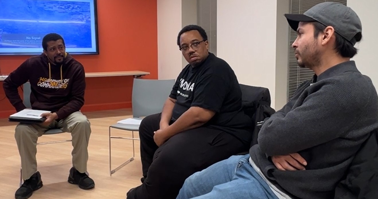 Three men sit and talk together.